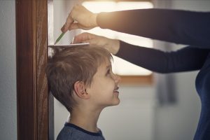 Mother measuring son's height and marking it with pencil on door.